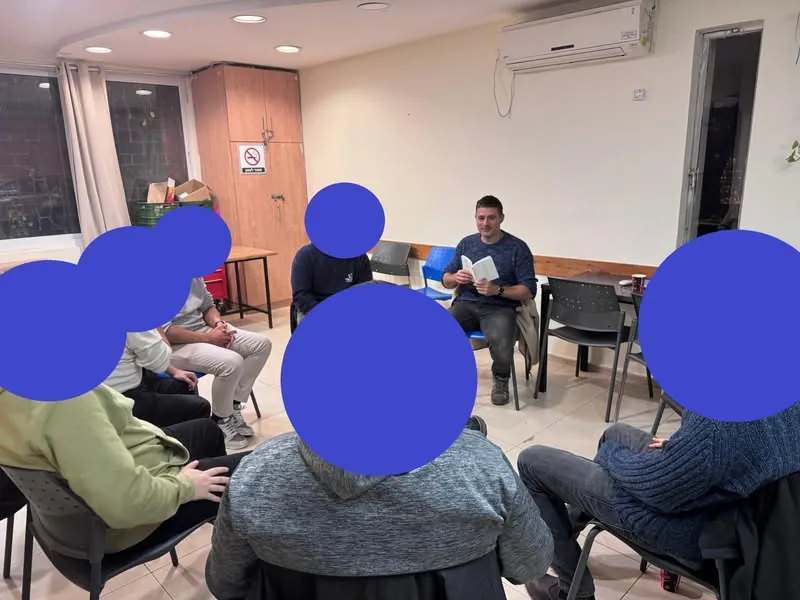 קבוצת גברים יושבת במעגל, גדעון איגרא מקריא מתוך ספר