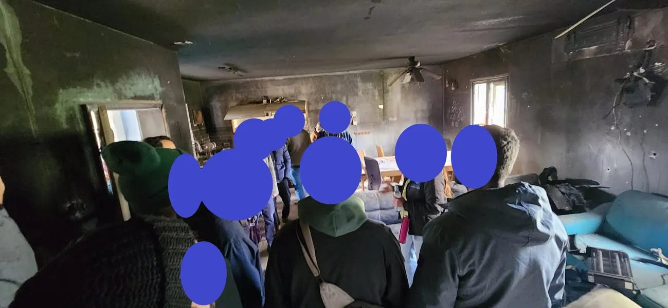 קבוצה עומדת בתוך בית שרוף בקיבוץ ניר עוז